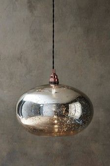 a shiny metal light hanging from a black cord on a gray wall with concrete walls in the background