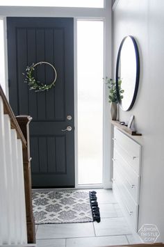 a black door with a wreath hanging on it's side next to a white staircase