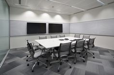 an empty conference room with white tables and gray chairs in front of two televisions