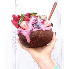 a person holding up a coconut bowl filled with fruit