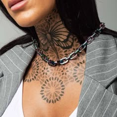 a woman with tattoos on her chest wearing a suit jacket and white tank top is looking at the camera