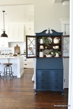 a blue china cabinet with white pumpkins and greenery on top in a kitchen