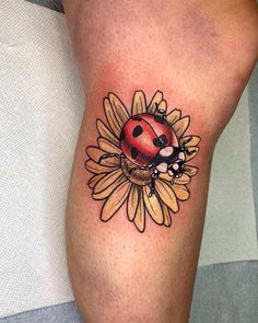 a ladybug tattoo on the leg of a person with sunflowers around it