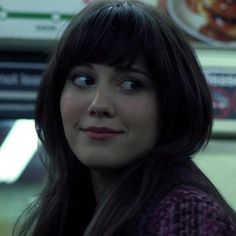 a woman with long black hair and bangs looks up at the camera in front of a fast food restaurant