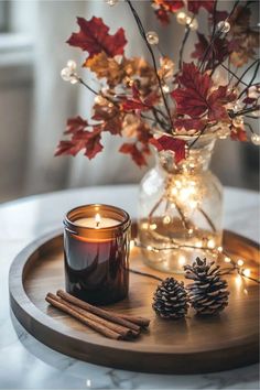 a wooden tray topped with a candle and some pine cones on top of a table