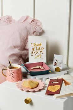 a desk with a pink pillow, card and other items on it next to a bed