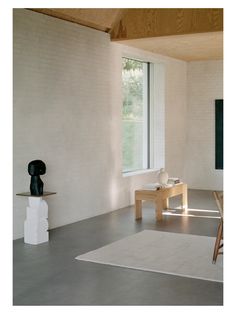 an empty room with a table, chair and vase on the floor in front of a large window