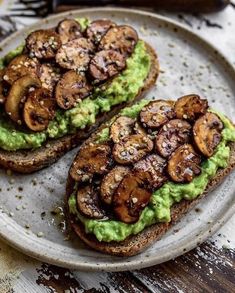 two pieces of bread with avocado and mushrooms on it sitting on a plate