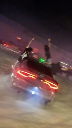 two people riding on the back of a red car in an open field at night