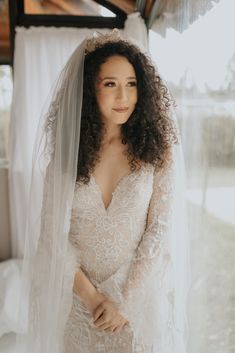 a woman wearing a wedding dress and veil standing in front of a window with her hands on her hips