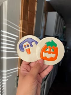 someone is holding up two buttons with faces on them in the shape of pumpkins