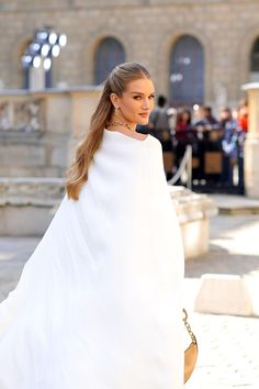 a woman in a white dress is walking down the street with her hair pulled back