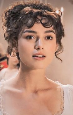 a woman with curly hair is looking at the camera while wearing a white dress and glasses