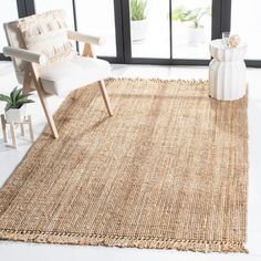 a white chair sitting on top of a rug in front of a large window next to a plant