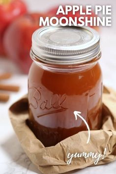 a glass jar filled with liquid sitting on top of a paper bag next to apples