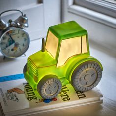 a green toy car sitting on top of a book next to an alarm clock and window