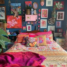 a bed covered in lots of colorful pillows and blankets next to a wall with pictures on it