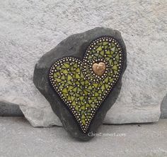 a heart shaped rock sitting on top of a gray stone covered in green and gold beads