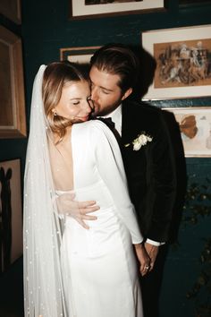 a bride and groom embracing each other in front of blue wall with pictures on it