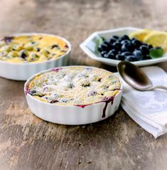 two bowls of blueberries and lemon on a wooden table with spoons next to them