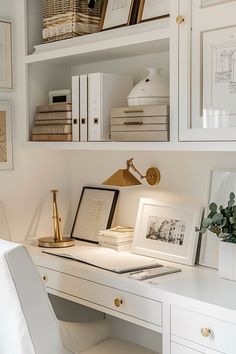 a white desk topped with a lamp next to a book shelf filled with books and pictures