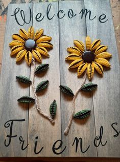 two sunflowers are sitting on top of a wooden sign that says welcome friends