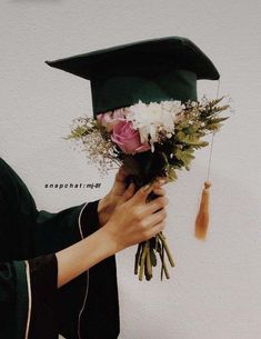 a person wearing a graduation cap and gown holding flowers in front of a white wall