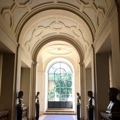 an arched hallway with statues on either side and a window in the middle that overlooks trees