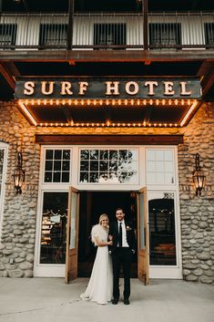 a bride and groom standing in front of the surf hotel on their wedding day at night