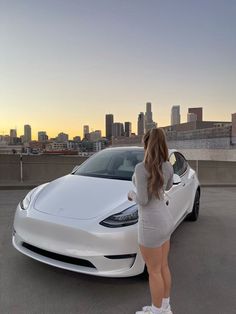 a woman standing next to a white car in front of a large cityscape