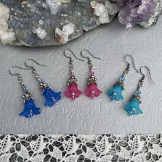 four pairs of dangling earrings with blue, pink and purple flowers on them next to a lace doily