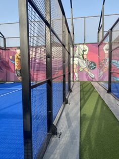 an indoor batting cage with artificial turf and painted mural on the wall behind it,