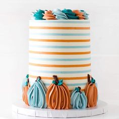 a multi - colored striped cake decorated with pumpkins and leaves on a white stand