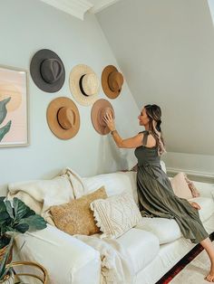 a woman sitting on top of a white couch in front of hats hanging on the wall