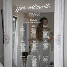 a wedding seating chart is shown in the reflection of a white framed mirror with a bride's dress on it