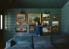 a woman standing next to a couch with paintings on the wall