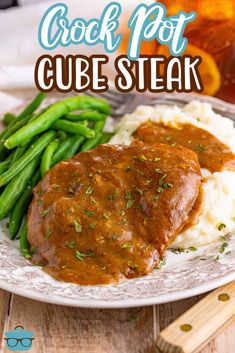 a white plate topped with meat covered in gravy next to green beans and mashed potatoes