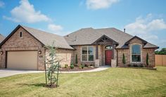 a brick house with two garages and a tree in the front yard on a sunny day