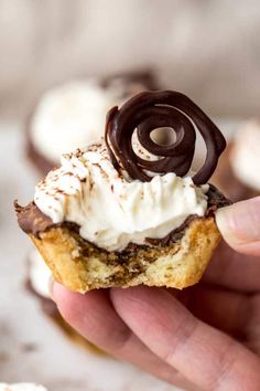 a hand holding a cupcake with whipped cream and chocolate