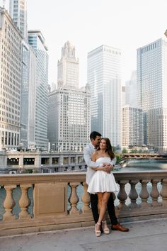 a man and woman standing next to each other on a bridge in front of tall buildings