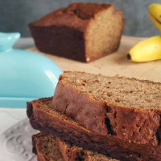 two slices of banana bread on a plate next to some bananas and a blue bowl