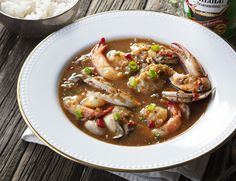 a white bowl filled with shrimp and rice next to a can of beer on a wooden table