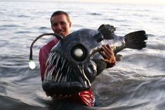 a man in the water holding a fish with its mouth open and it's tongue out