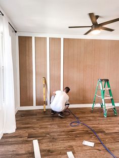 a man that is kneeling down on the floor in front of a ladder and paint roller