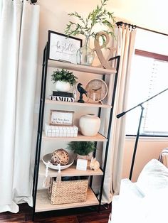 a bookshelf with plants and other items on it in front of a window