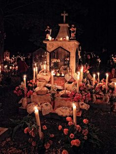 candles are lit in front of a small shrine with statues and flowers on the ground