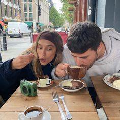 a man and woman sitting at a table with food in front of them, eating cake