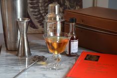 a table topped with bottles and glasses next to a metal cup filled with liquid on top of a marble counter