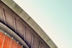 an airplane is flying in the sky over a building with a curved roof and orange walls