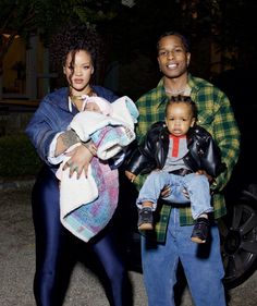 a man and two women holding babys in their arms while standing next to a car